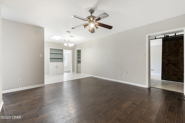 unfurnished living room with ceiling fan with notable chandelier, wood-type flooring, built in features, and a barn door