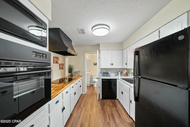 kitchen featuring light hardwood / wood-style flooring, white cabinetry, black appliances, a textured ceiling, and exhaust hood