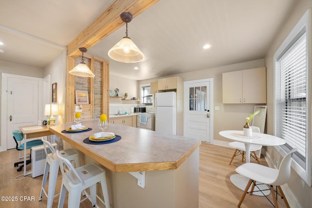 kitchen with a breakfast bar area, decorative light fixtures, light hardwood / wood-style flooring, white appliances, and beam ceiling