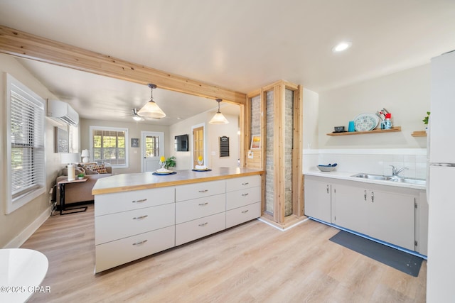 kitchen featuring sink, decorative light fixtures, light wood-type flooring, a wall unit AC, and white cabinets