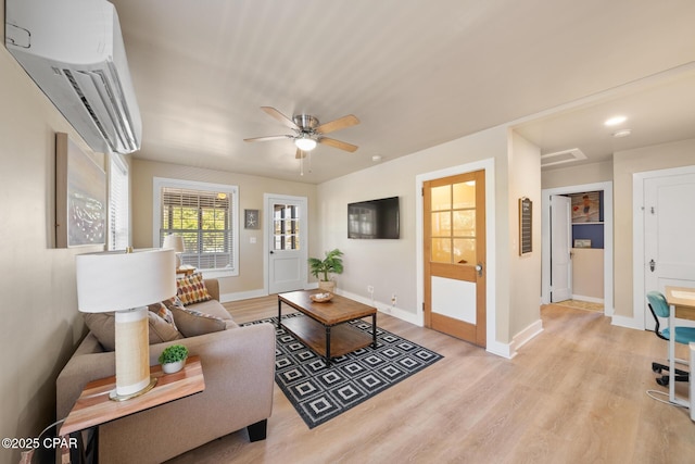 living room with ceiling fan, a wall mounted AC, and light wood-type flooring