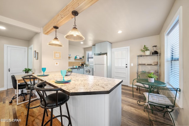 kitchen featuring a kitchen bar, beamed ceiling, dark hardwood / wood-style flooring, white fridge, and pendant lighting