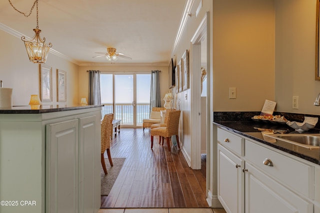 kitchen with wood finished floors, a sink, white cabinets, ornamental molding, and pendant lighting