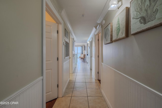 hall with a wainscoted wall, crown molding, and light tile patterned flooring