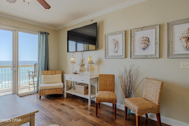 sitting room with a water view, baseboards, ornamental molding, and wood finished floors