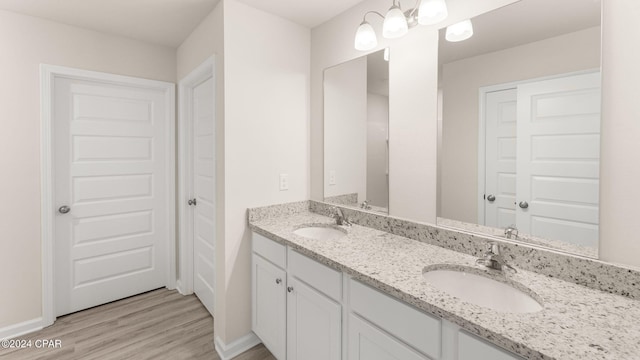 bathroom featuring double vanity, wood finished floors, baseboards, and a sink