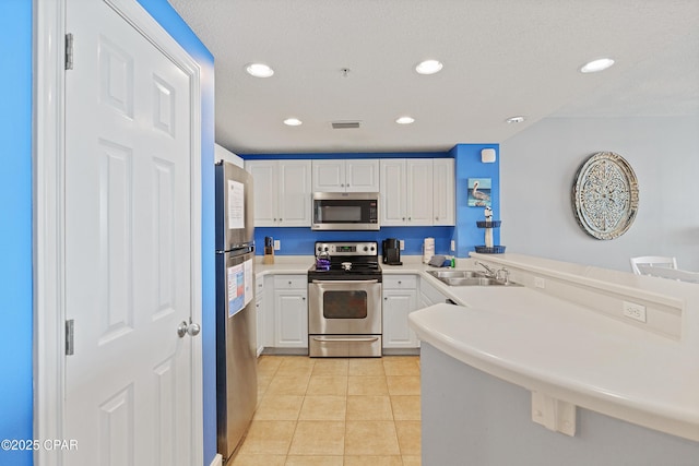 kitchen featuring light tile patterned floors, a peninsula, a sink, appliances with stainless steel finishes, and white cabinetry