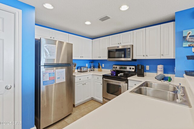 kitchen with visible vents, a sink, stainless steel appliances, white cabinets, and light tile patterned floors