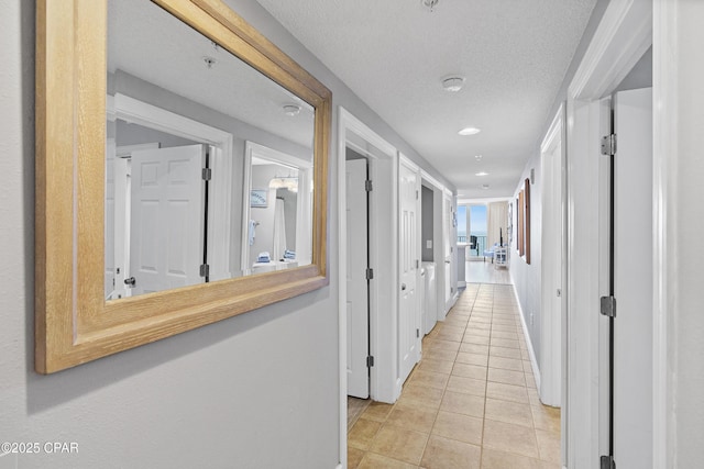 hallway with recessed lighting, baseboards, a textured ceiling, and light tile patterned flooring