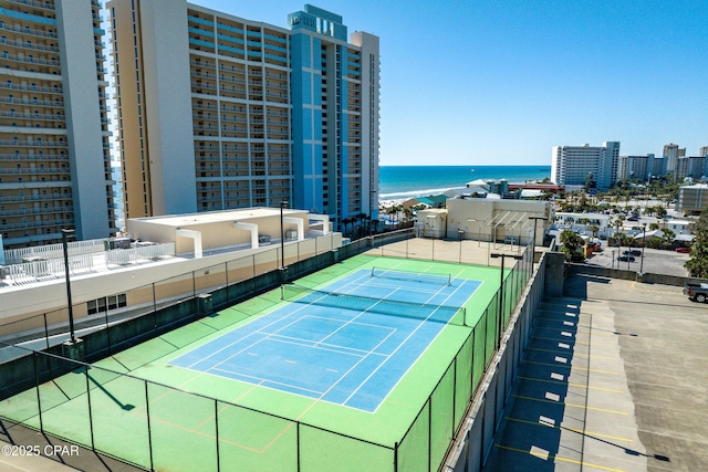 view of tennis court featuring a city view, fence, and a water view