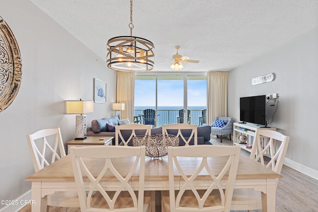 dining room with ceiling fan with notable chandelier, a textured ceiling, baseboards, and wood finished floors