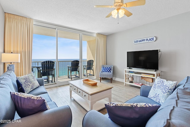 living area featuring a wall of windows, a ceiling fan, wood finished floors, baseboards, and a textured ceiling