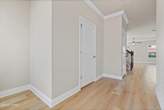 corridor featuring light wood-style floors, baseboards, ornamental molding, and visible vents