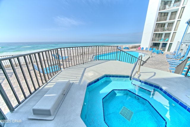 view of swimming pool featuring a community hot tub, a water view, and a view of the beach