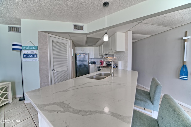 kitchen featuring visible vents, white cabinets, freestanding refrigerator, hanging light fixtures, and a sink