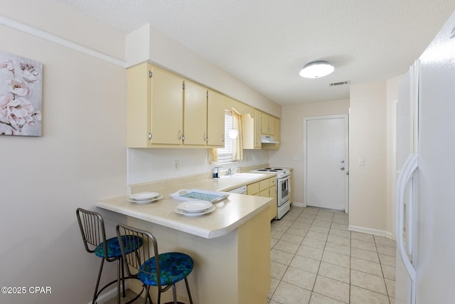 kitchen with white appliances, visible vents, light countertops, under cabinet range hood, and a kitchen breakfast bar