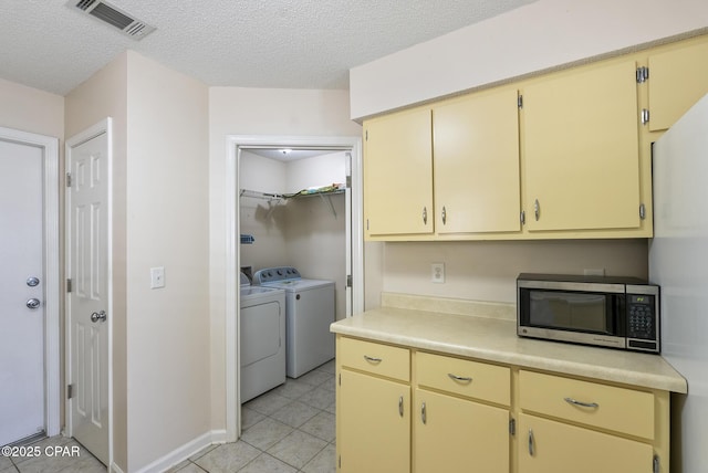 kitchen with stainless steel microwave, light countertops, cream cabinets, light tile patterned flooring, and separate washer and dryer