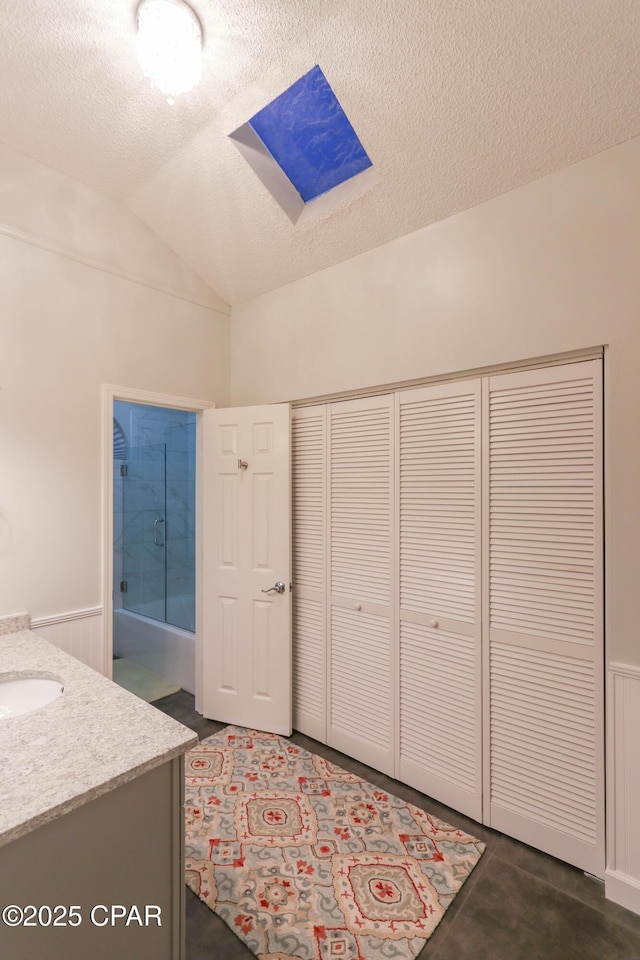 full bath featuring vanity, vaulted ceiling with skylight, a wainscoted wall, and a textured ceiling