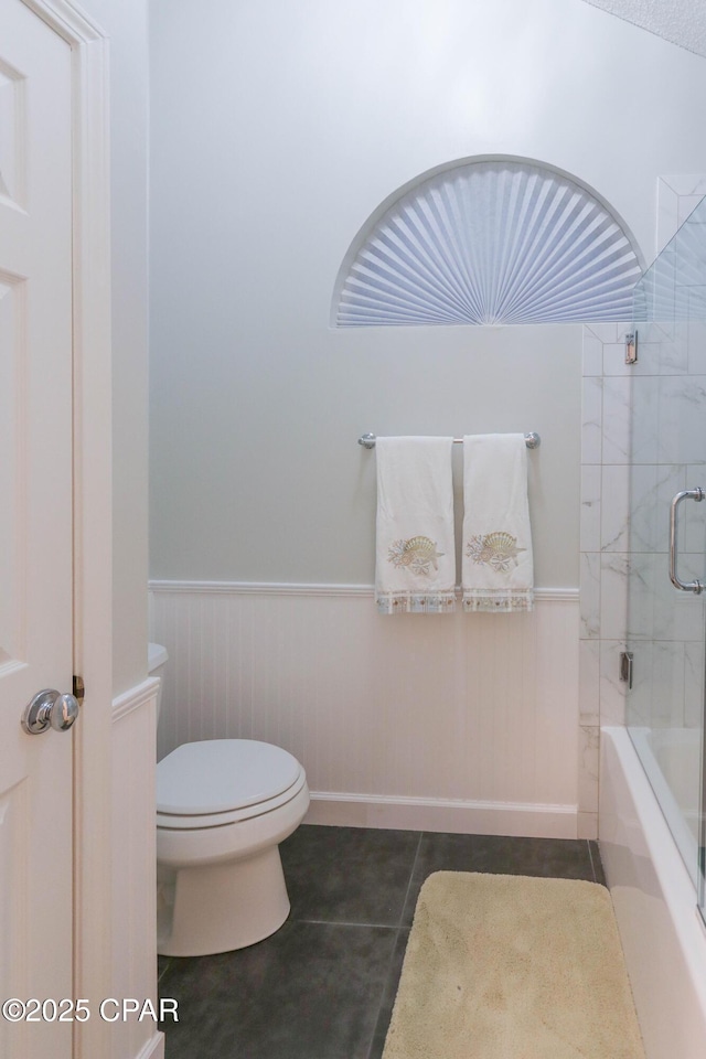 full bath featuring tile patterned floors, toilet, shower / bath combination with glass door, and wainscoting