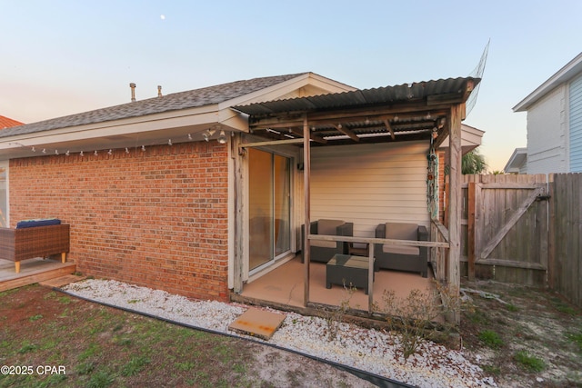 rear view of house featuring a patio, brick siding, roof with shingles, and fence