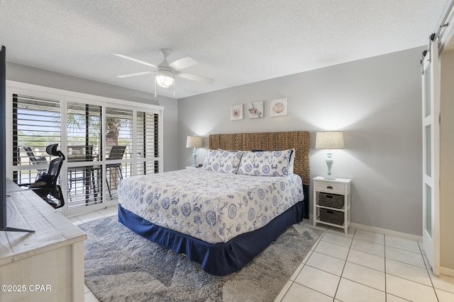 bedroom featuring ceiling fan, a textured ceiling, light tile patterned flooring, access to outside, and a barn door