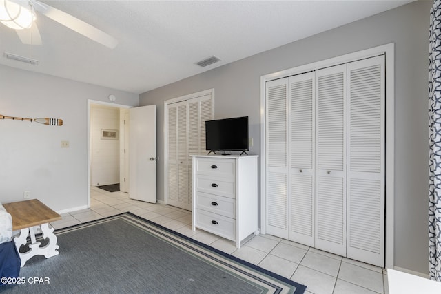 unfurnished bedroom featuring multiple closets, light tile patterned floors, a textured ceiling, and ceiling fan