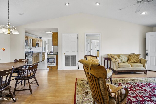 living room featuring ceiling fan with notable chandelier, vaulted ceiling, heating unit, and light wood-type flooring