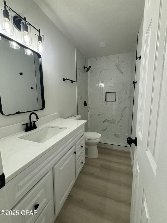 bathroom featuring vanity, a tile shower, toilet, and hardwood / wood-style floors