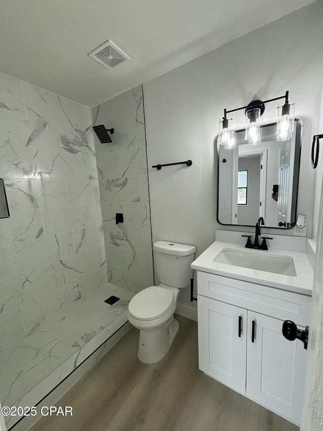 bathroom with a tile shower, vanity, hardwood / wood-style floors, and toilet