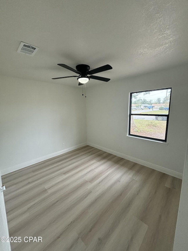 spare room featuring light wood-type flooring, ceiling fan, and a textured ceiling