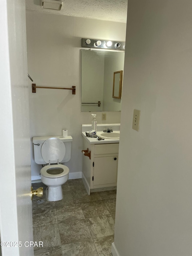 half bathroom with baseboards, vanity, and toilet