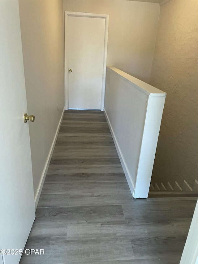 corridor featuring a textured wall, baseboards, dark wood-type flooring, and an upstairs landing