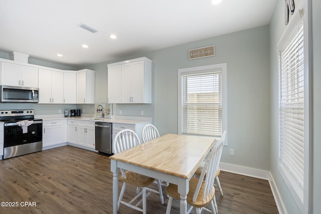 kitchen featuring dark wood-type flooring, a sink, appliances with stainless steel finishes, white cabinets, and baseboards