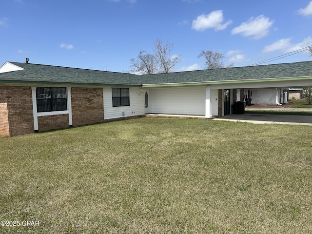 back of property with brick siding, roof with shingles, an attached carport, and a yard