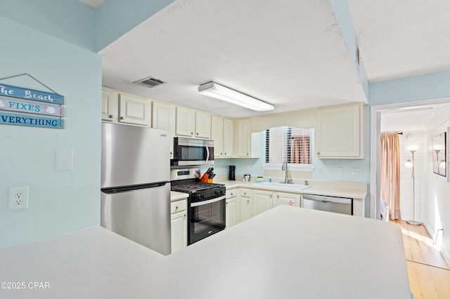 kitchen with cream cabinetry, stainless steel appliances, sink, and light wood-type flooring