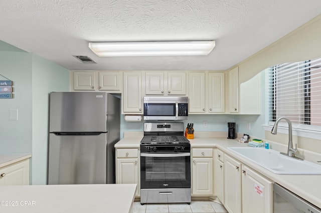 kitchen with stainless steel appliances, sink, light tile patterned floors, and a textured ceiling