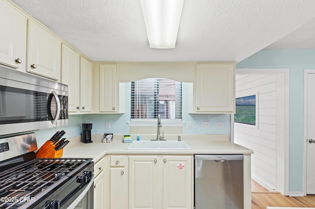 kitchen with appliances with stainless steel finishes, sink, light hardwood / wood-style floors, a textured ceiling, and cream cabinetry