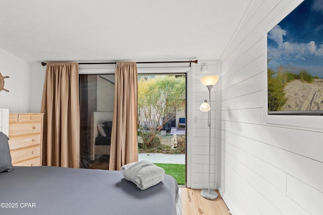 bedroom with access to outside, wooden walls, and wood-type flooring