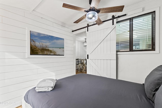 bedroom featuring crown molding, ceiling fan, a barn door, and wood walls