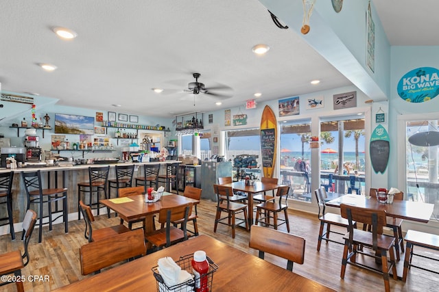 dining room featuring bar, ceiling fan, and light wood-type flooring