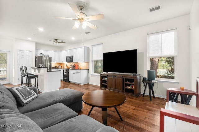 living room featuring a ceiling fan, wood finished floors, visible vents, and baseboards