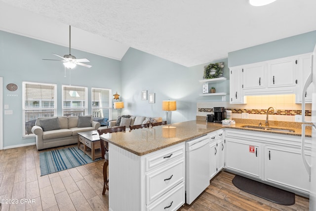 kitchen with wood finished floors, white cabinetry, white dishwasher, a sink, and light stone countertops