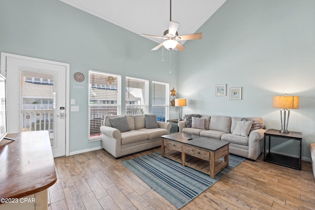 living area with baseboards, ceiling fan, a high ceiling, and wood finished floors