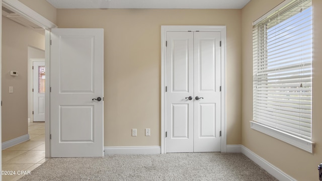 unfurnished bedroom featuring light carpet, baseboards, a closet, and light tile patterned flooring