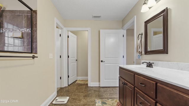 bathroom with a textured ceiling, vanity, visible vents, and baseboards