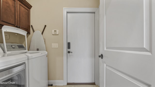 clothes washing area featuring washing machine and dryer, cabinet space, and baseboards