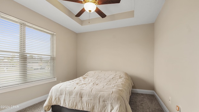 bedroom with a tray ceiling, carpet, a ceiling fan, and baseboards