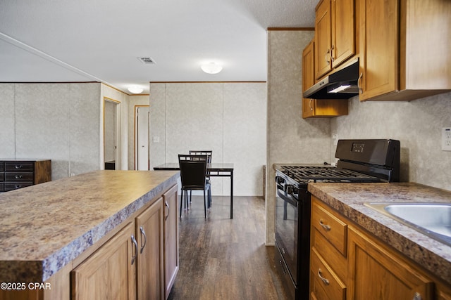kitchen featuring black gas range oven, under cabinet range hood, visible vents, dark wood-type flooring, and crown molding