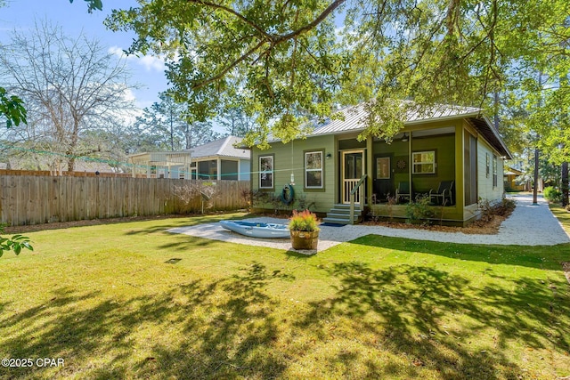 rear view of property with metal roof, a lawn, fence, and a sunroom