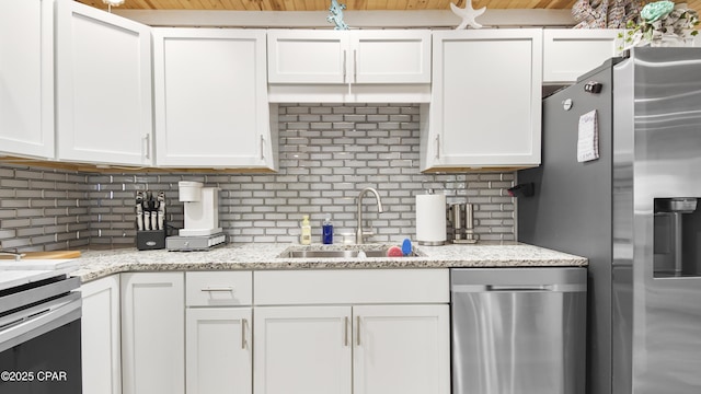 kitchen featuring a sink, light stone countertops, stainless steel appliances, white cabinetry, and backsplash